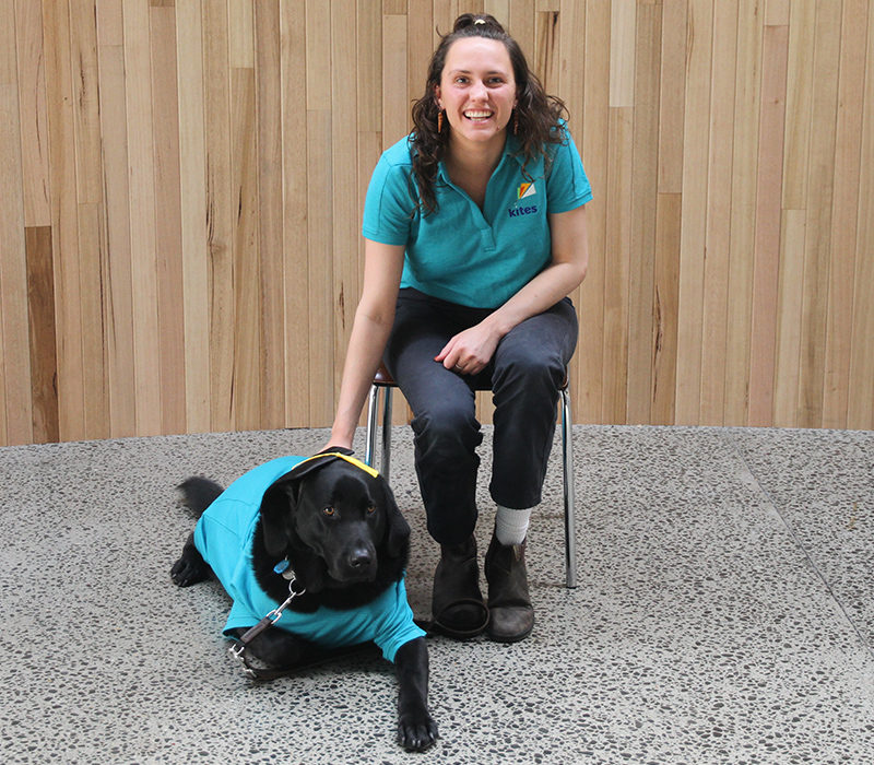 Smiling lady with a black dog wearing a motarboard
