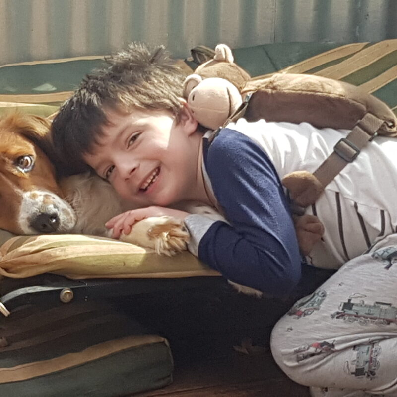 Little boy smiling, and laying next to a pet dog