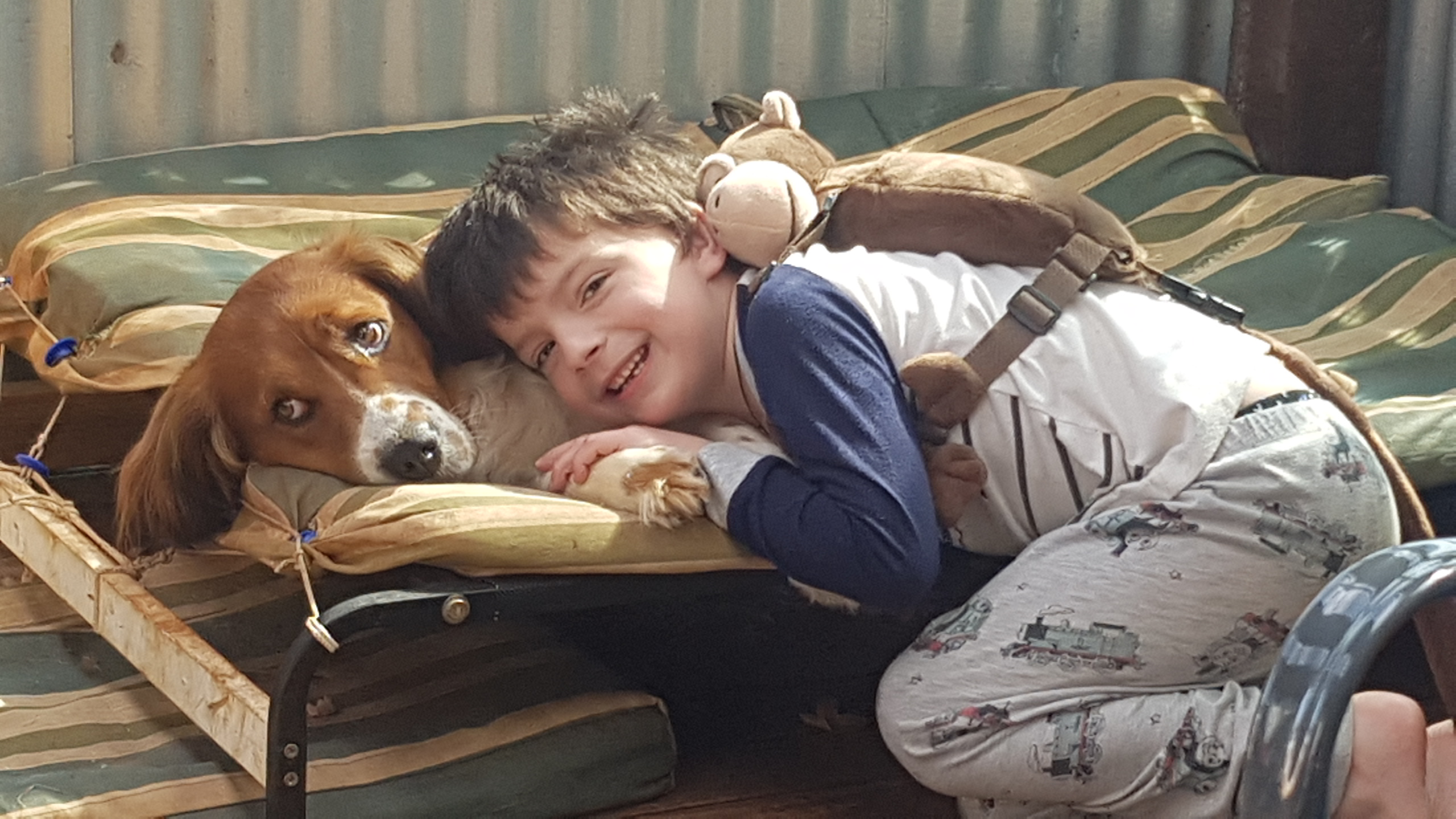 Little boy smiling, and laying next to a pet dog