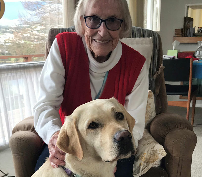 a smiling lady sitting behind a dog