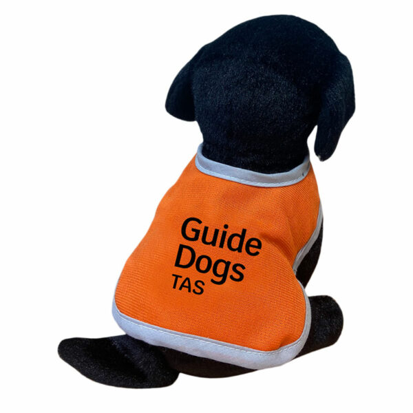 Black plush puppy toy with orange jacket that reads Guide Dogs Tas