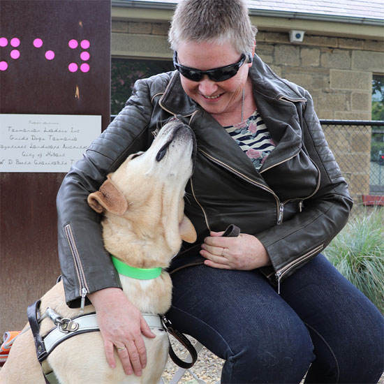 Woman in leather jacket sits with her yellow Guide Dog in harness