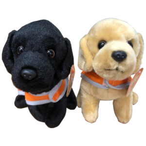 One black and one blonde soft toy in the shape of a labrador puppy, facing the camera. They have orange Guide Dog training coats.